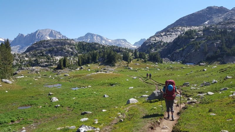 three backpackers cross a high mountain meadow on a hiking adventure.