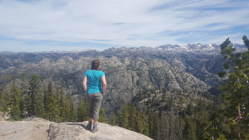 A hiker is rewarded with a wide open view of snow-capped mountains and craggy hills. 