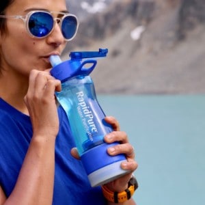 Person sips from a RapidPur bottle with lake in the background.