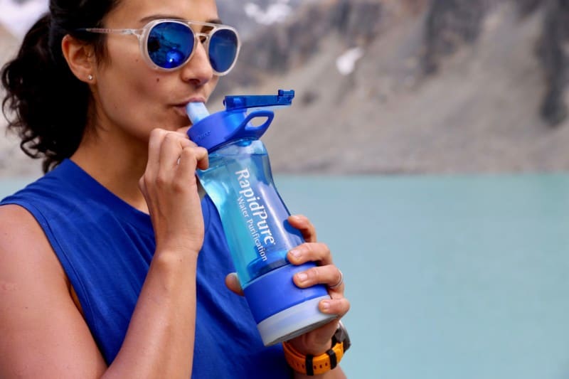 Person sips from a RapidPur bottle with lake in the background.