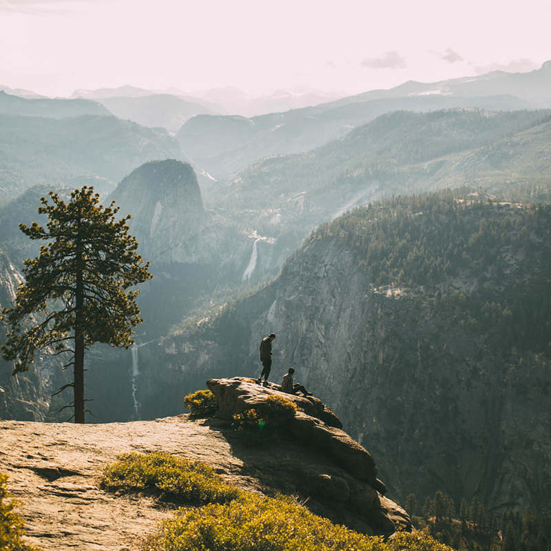 two hikers rest on a rock above a valley with waterfalls
