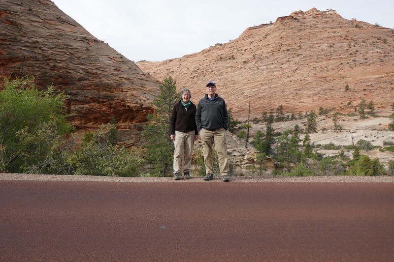 Two people stand on the side of a trail in front of desert hills in the Grand Canyon.