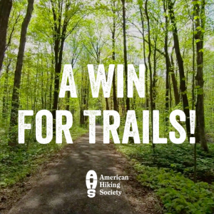 Background image of tree lined trail with text overlay "A Win for Trails" with American Hiking Society logo below text.