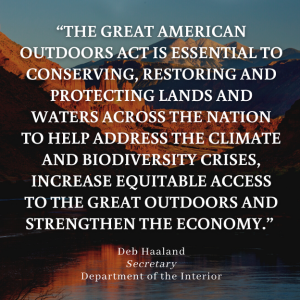 Background image of an alpine lake with mountains beyond it. Text overlay reads: "The Great American Outdoors Act is essential to conserving, restoring and protecting lands and waters across the nation to help address the climate and biodiversity crises, increase equitable access to the great outdoors and strengthen the economy". The quote is attributed to Deb Haaland, Secretary for the Department of the Interior.