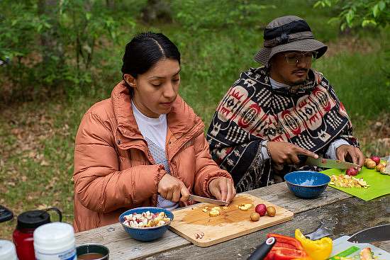 two participants prep a meal by chopping veggies at a picnic table