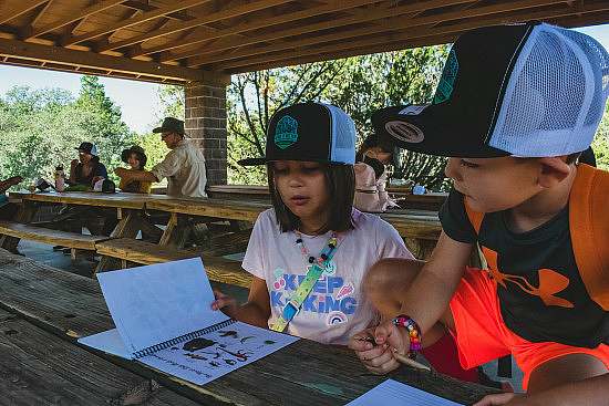 two kids in "Leave it Better"hats flip through an outdoor identification workbook