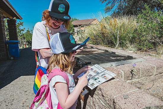 Person with red hair smiles big while a kid flips through a plant identification booklet with a purple flower next to a retaining wall