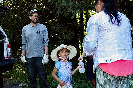 A forest service employee speaks while a young event participant in a wide brim hat looks into the camera