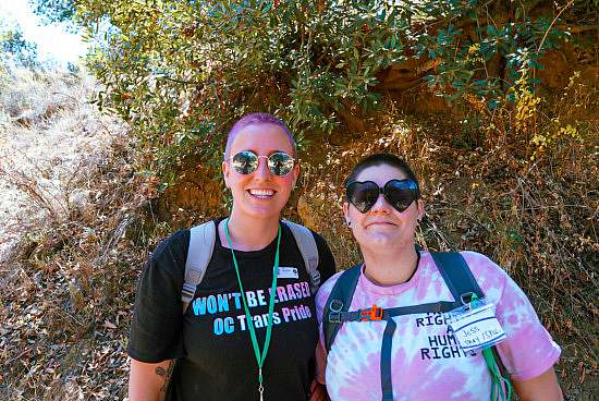 Two hikers with packs and sun glasses smile for the camera while pausing in a shady section of trail