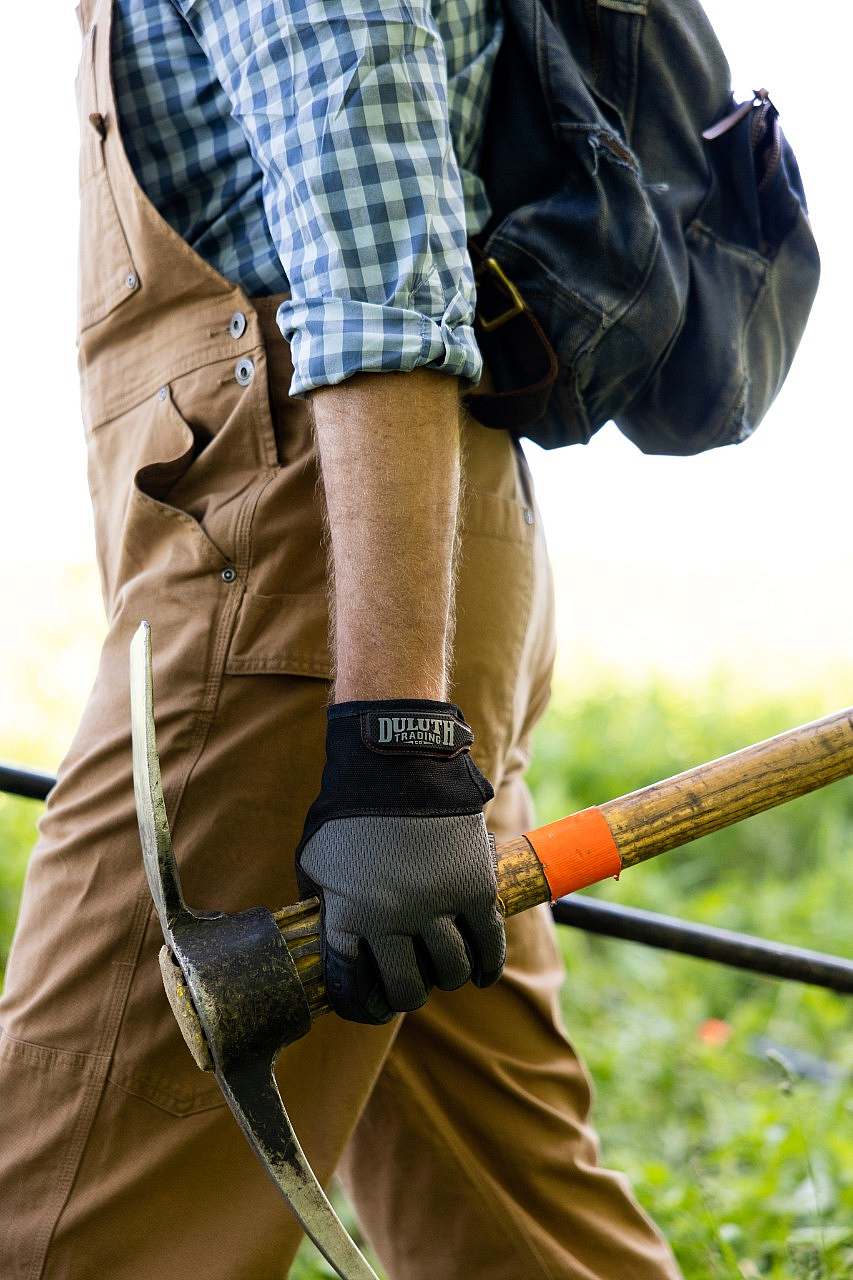 Close up os a volunteer caryying a pick mattock wearing Duluth Trading work gloves