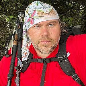 Ronald Morris outdoor hiking self portrait with backpack, trekking poles, and a white illustrated buff on his head.