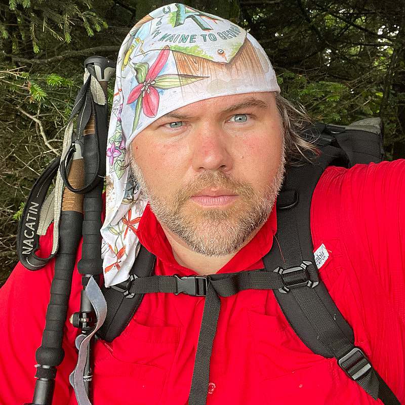 Ronald Morris outdoor hiking self portrait with backpack, trekking poles, and a white illustrated buff on his head.