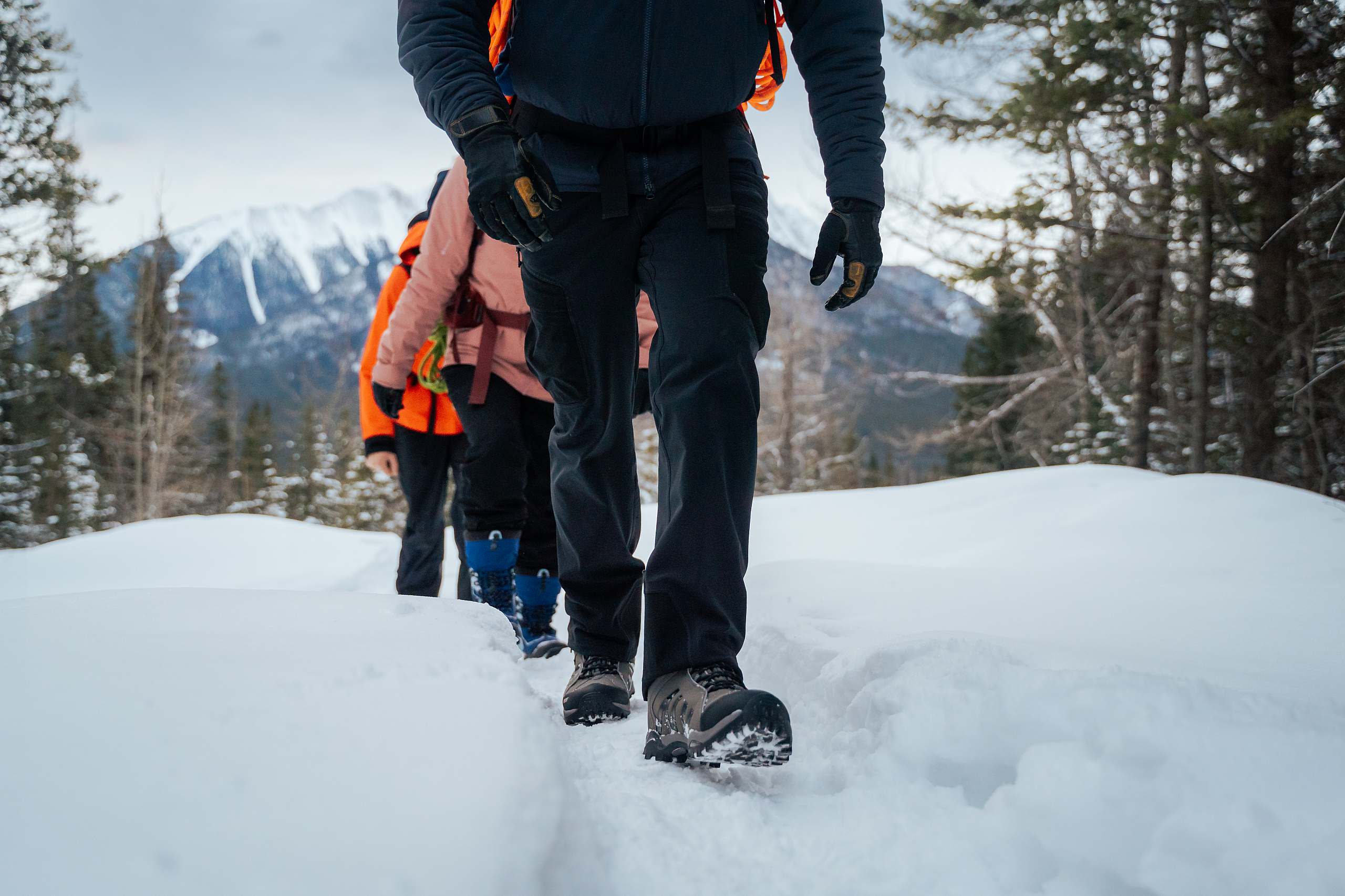 close up of the boots of a group of hikers walking in a snowy field.