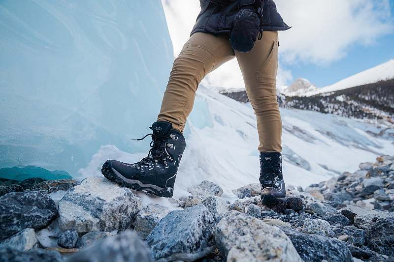 Close up of Baffin boots of someone walking across rocks in front of a wall of ice.