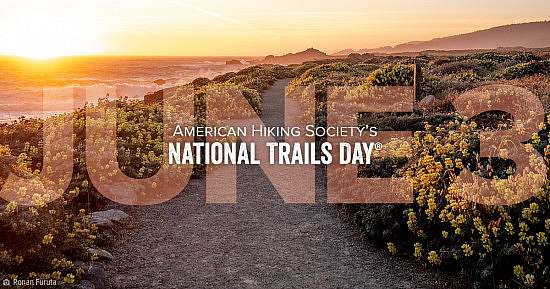 American Hiking Society's National Trails Day June 3 wordmark over lay on gravel trail winding through flowering bushes near a coastline as the sun sets.