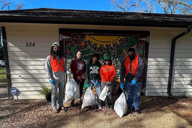 Group of volunteers hold trash bags in front of a small building
