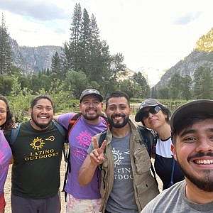 group of hikers wearing Latino Outdoors shirts smile for a selfie photo in a meadow.