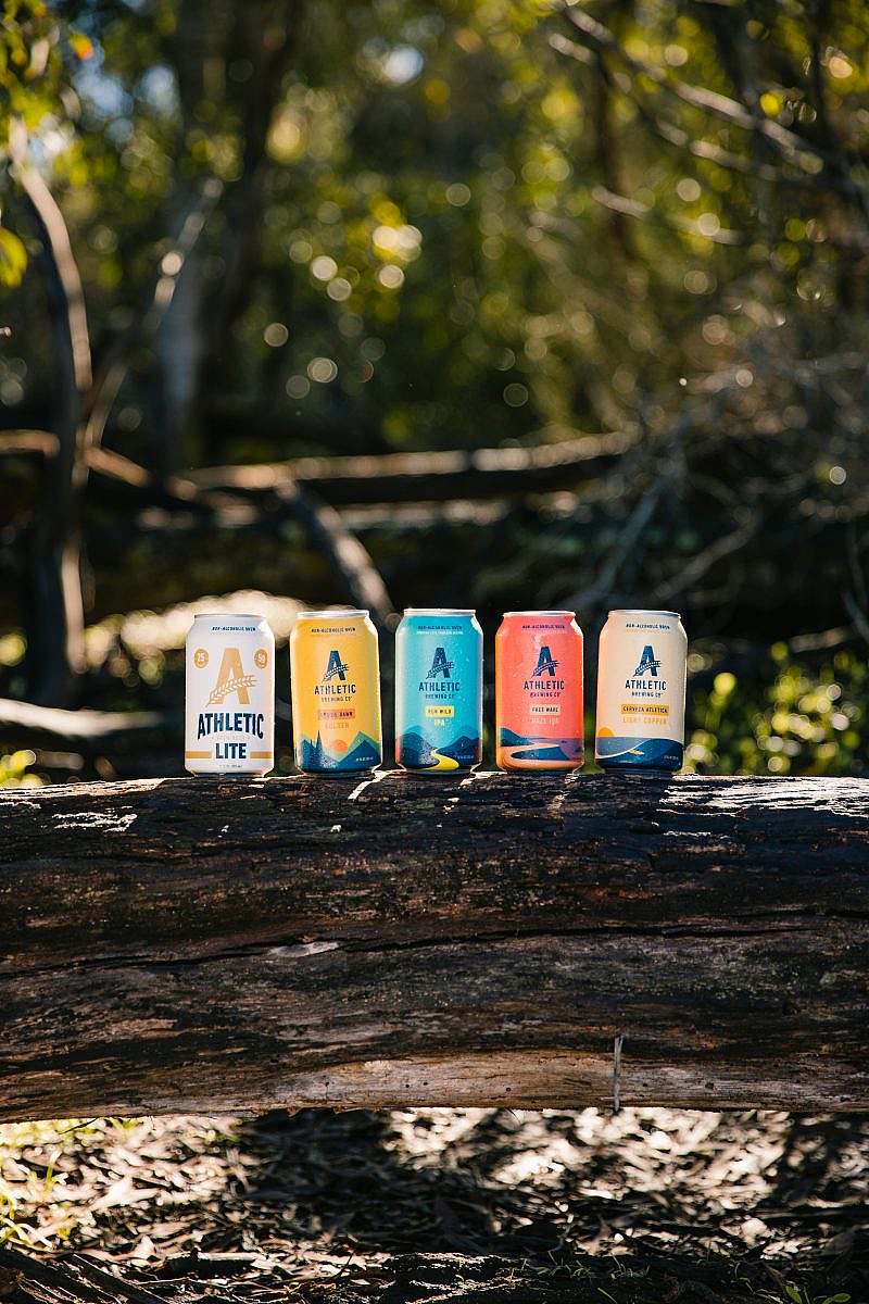 Five cans of Athletic Brewing in varying colors are positioned together on a tree.