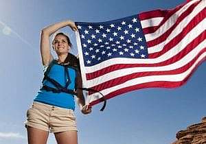 An attractive young woman on a hike in the desert holding a U.S. flag as it blows in the wind.